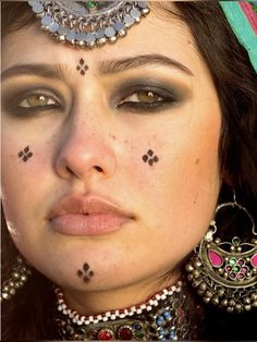 a close up of a woman with makeup and jewelry on her face, looking at the camera