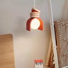 an orange and white lamp hanging from a ceiling next to a wooden chair with a book on it