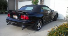 a black sports car is parked in front of a garage with flowers on the driveway