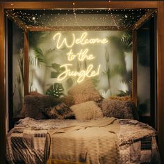 a welcome to the jungle neon sign above a bed with pillows and blankets on it