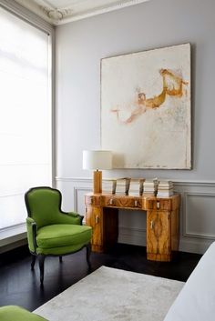 a green chair sitting in front of a painting on the wall next to a desk