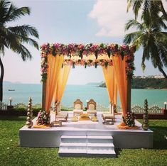 an outdoor ceremony set up with flowers and orange draping on the grass by the ocean