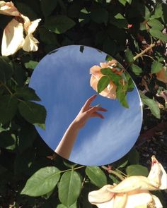 a person's hand reaching up into the sky in front of a round mirror