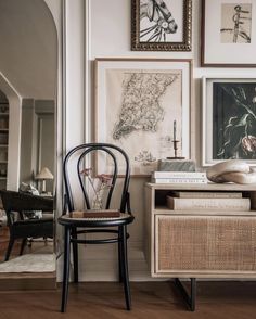 a chair sitting next to a table with pictures on the wall above it and other furniture