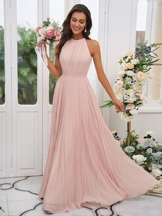 a woman in a long pink dress standing next to a flower arrangement and holding a bouquet