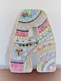 a decorative letter made out of mosaic tiles on a wooden table with a white wall in the background