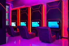 a room with chairs, televisions and neon colored lighting on the walls in front of them