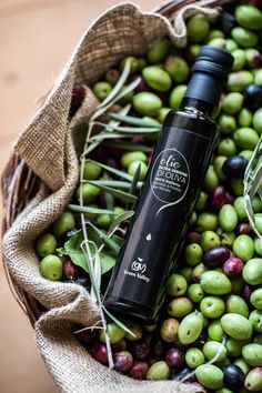 a bottle of olive oil sitting on top of a basket filled with green and black olives