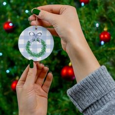 a person holding up a christmas ornament in front of a christmas tree