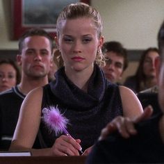 a woman sitting in front of a group of people with a feather on her finger