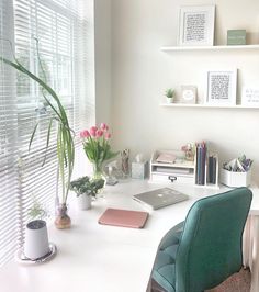 a white desk topped with a laptop computer next to a green chair and potted plant