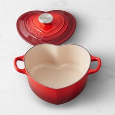 a red pot with a heart shaped lid sitting on top of a white countertop