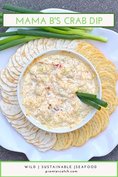 a white plate topped with crackers next to a bowl of crab dip and asparagus