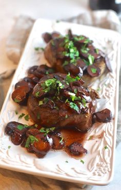 two pieces of meat covered in mushrooms on a white plate with garnishes