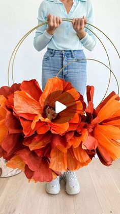 a woman standing in front of an orange flower arrangement with hoop holding it up to her face