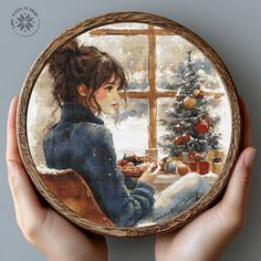 a person holding up a cross - stitch picture in their hand with a christmas tree on the window sill