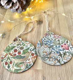 two ceramic ornaments are sitting on a wooden table next to pine cones and christmas lights