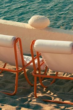 two beach chairs sitting on the sand next to water and an object that looks like a ball