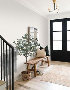 a wooden bench sitting in front of a black door next to a plant on top of a table