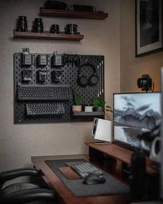 a desk with a computer monitor, keyboard and headphones hanging on the wall above it