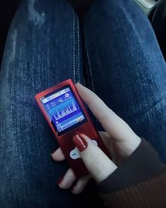 a person holding a red cell phone in their left hand while sitting on the floor