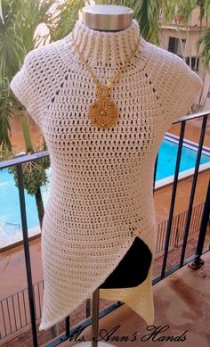 a white crocheted top with a gold necklace on it and a pool in the background