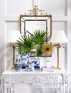 a white table topped with blue and white vases next to a mirror on top of a wall