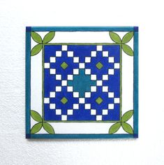 a blue and white square with green leaves on the edge is mounted to a wall