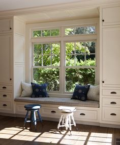 a window seat in the corner of a room with two stools and pillows on it