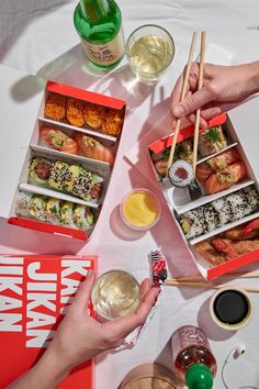 two people holding chopsticks over an assortment of sushi and other food items