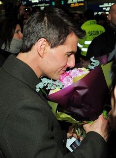 a man is holding flowers in his hand and looking down at the ground while people are standing around him