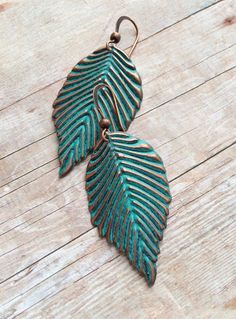 two green leaf shaped earrings sitting on top of a wooden table