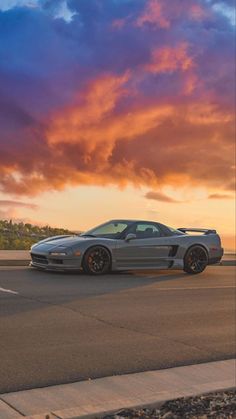 a silver sports car parked on the side of the road in front of a sunset