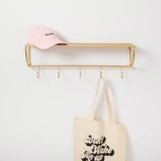 a tote bag hanging on a wall next to a coat rack with a pink hat