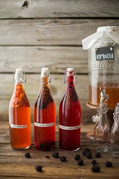 three bottles filled with liquid sitting on top of a wooden table next to some blackberries