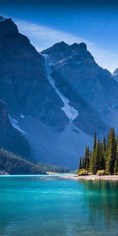 the mountains are covered in snow and pine trees, along with clear blue lake water