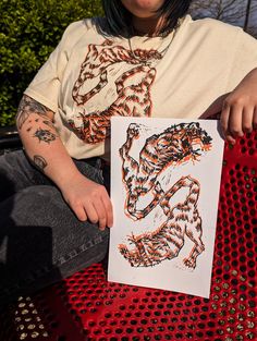 a woman sitting on top of a red bench holding up a piece of paper with an animal drawn on it