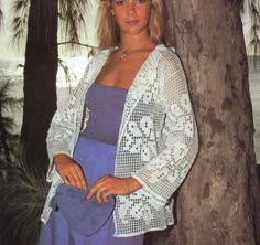 a woman standing next to a tree wearing a blue dress and white cardigan sweater