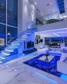 a modern living room with blue lighting and white furniture in the center, along with stairs leading up to an open floor plan