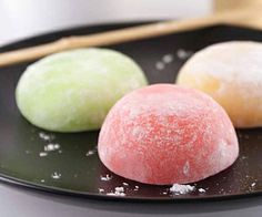 three different types of doughnuts on a black plate with chopsticks next to them