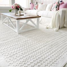 a living room with white furniture and pink flowers on the coffee table in front of it