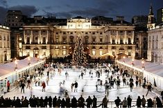 people skating on an ice rink at night in front of a large building with a christmas tree