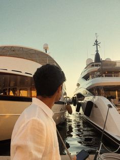 a man standing next to a boat in the water with another boat docked behind him