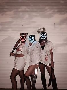 three women in white outfits with neon masks on their faces and one holding a knife