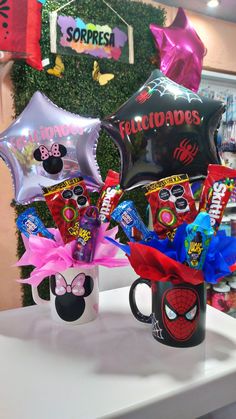 two coffee mugs filled with balloons and some kind of candy in front of a wall