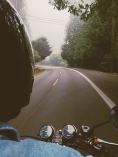 a person riding a motorcycle down a curvy road with trees in the background