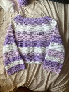 a purple and white sweater sitting on top of a bed next to a ball of yarn