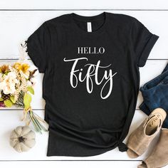 a black t - shirt with the words hello fifty on it next to some flowers