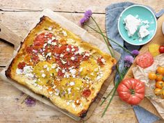 a square pizza with tomatoes, cheese and other toppings next to it on a cutting board