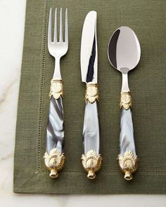 three silver and gold utensils sitting on top of a green napkin